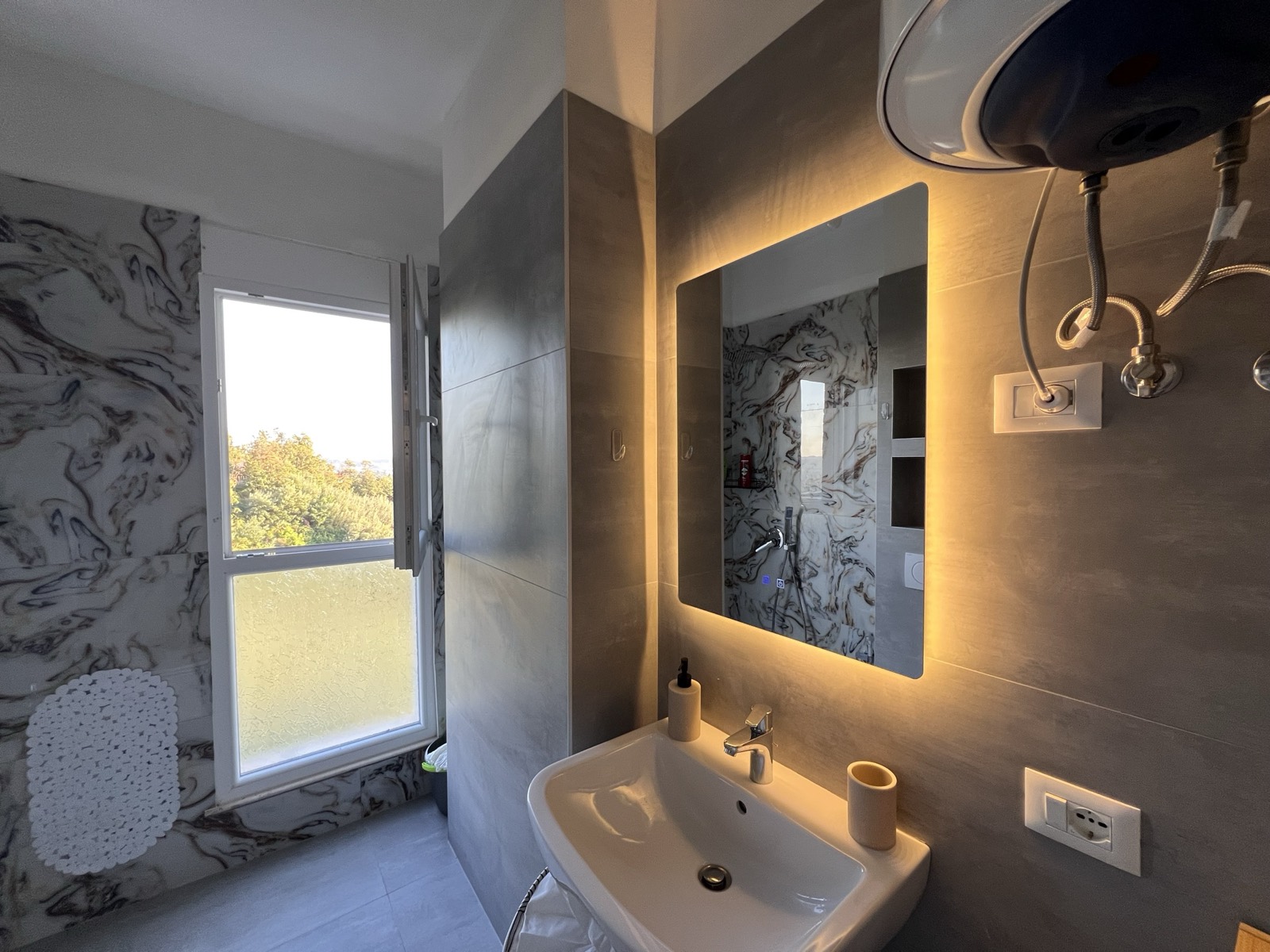 Modern bathroom with marble-effect tiling, a backlit mirror and a window over the trees